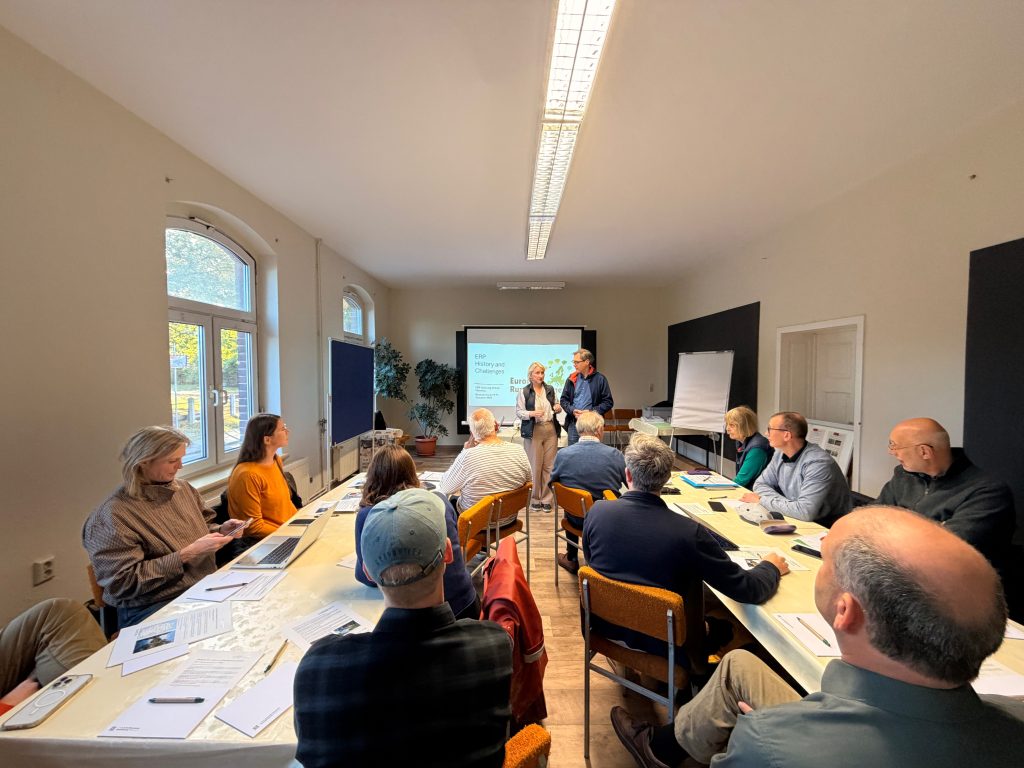 Two people present a slide titled ERP History and Challenges to a group of attendees seated at a U-shaped conference table.