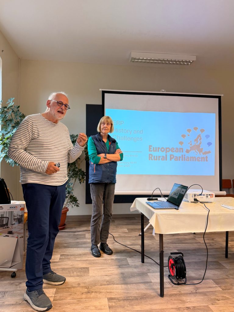 A man and a woman standing in front of a projection screen displaying European Rural Parliament: History and Challenges.